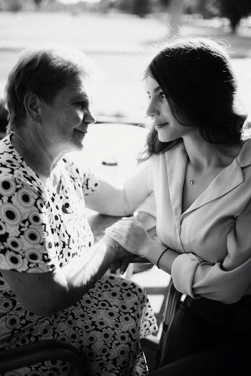 Photo en noir et blanc d'une femme âgée et d'une jeune femme assises face à face, qui se tiennent la main et se sourient