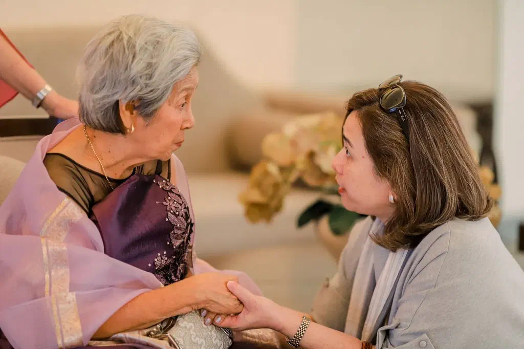 Une femme tient la main de sa mère âgée pendant une conversation, dans un salon