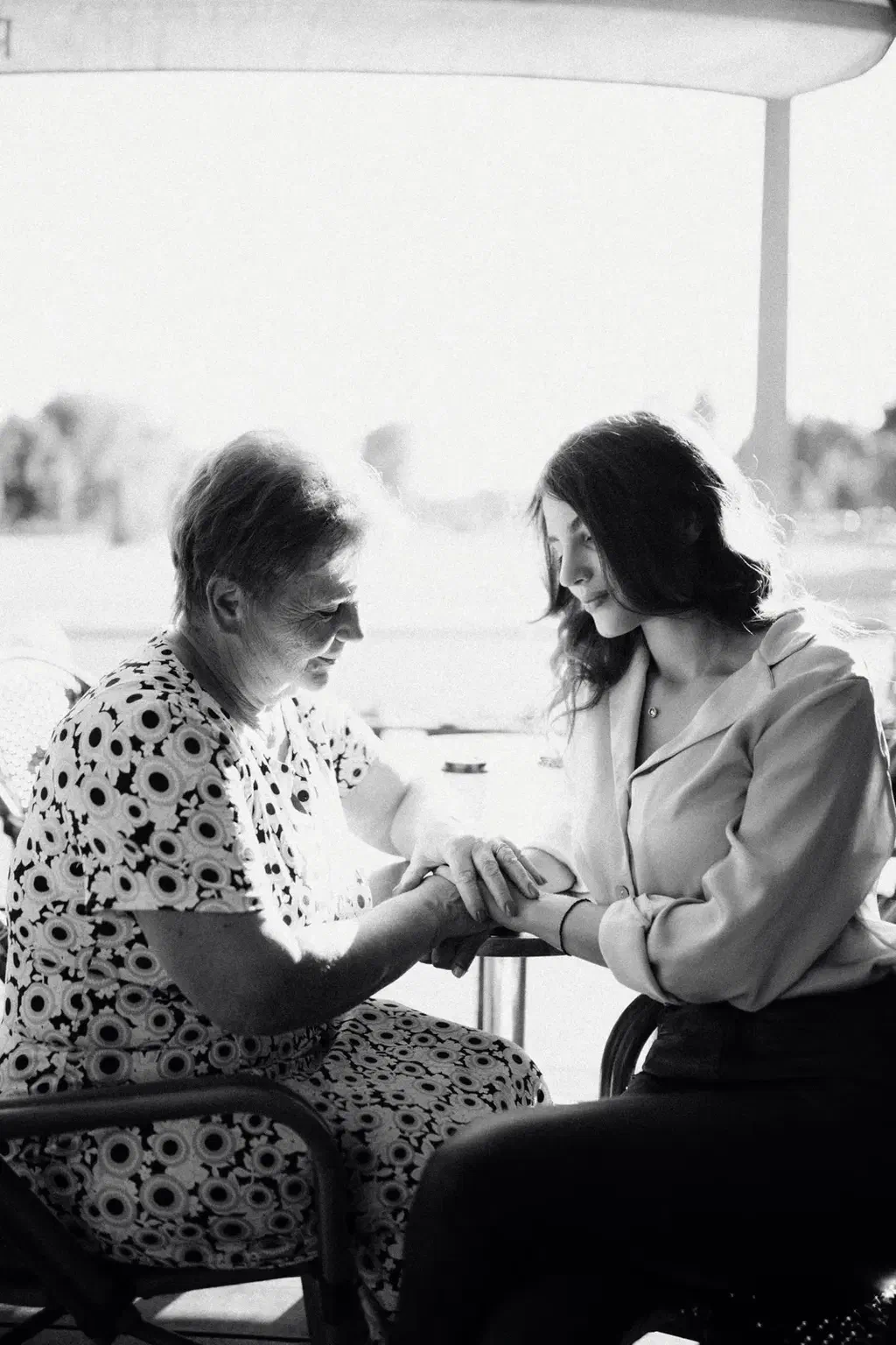 Photo en noir et blanc d'une femme âgée et d'une jeune femme assises face à face, qui se tiennent les mains