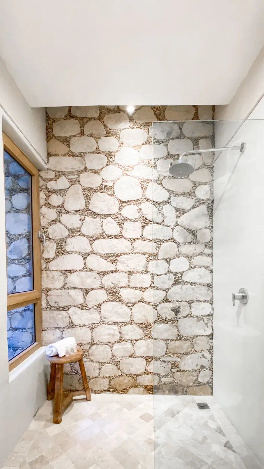 Une douche de plain-pied sans rebord, avec un tabouret en bois posé à côté