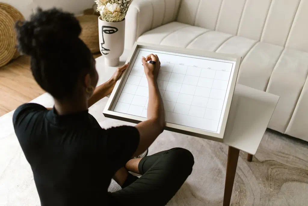 Une femme assise au sol chez elle, un grand calendrier posé devant elle