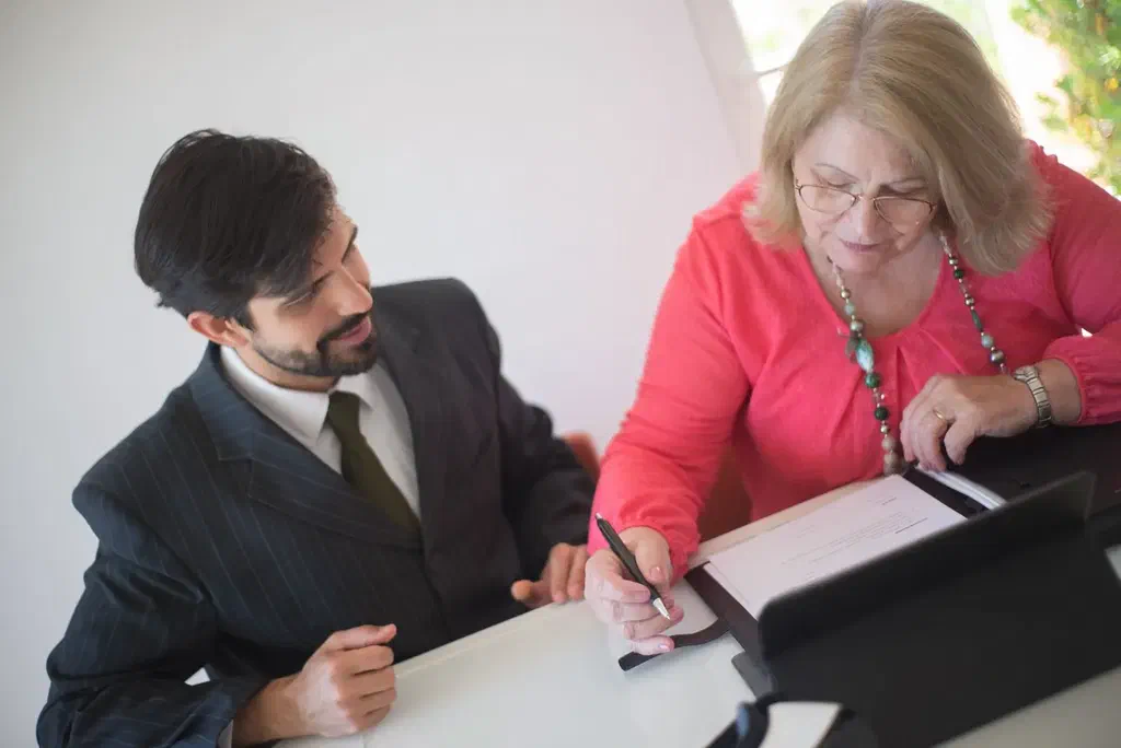 Une femme âgée signe des documents avec l'aide d'un conseiller