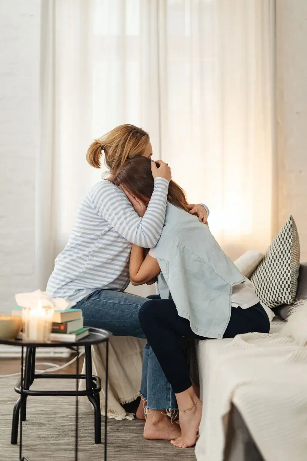 Une femme et sa mère âgée s'enlacent près d'une fenêtre, dans un salon clair