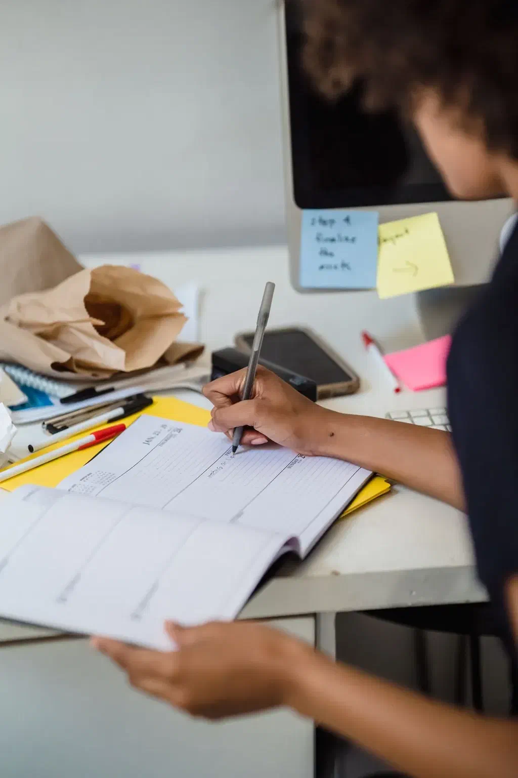 Un agenda ouvert sur un bureau, une main en train d'y écrire